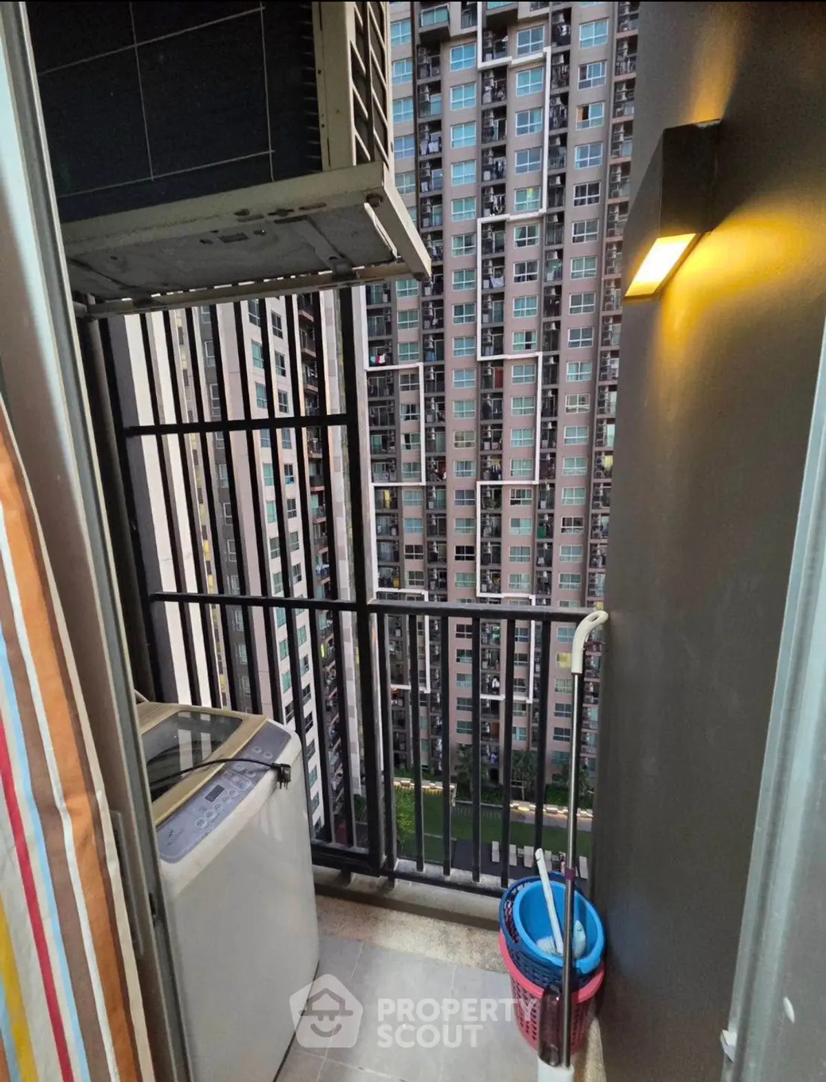 Compact balcony with washing machine and city view in high-rise apartment.