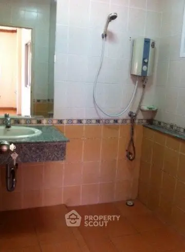 Compact bathroom with wall-mounted shower and sink in tiled setting.