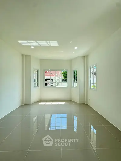 Spacious sunlit room with glossy tiled floors and large windows in modern home.