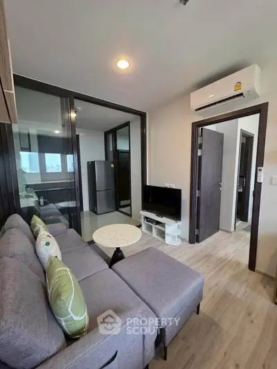 Modern living room with sleek design, featuring a cozy gray sofa, flat-screen TV, and air conditioning unit.