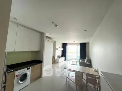 Modern open-plan living room with dining area and washing machine, featuring large windows and natural light.