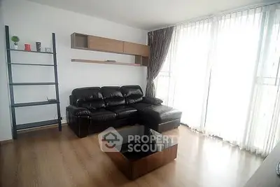 Modern living room with sleek black leather sofa and large windows for natural light.