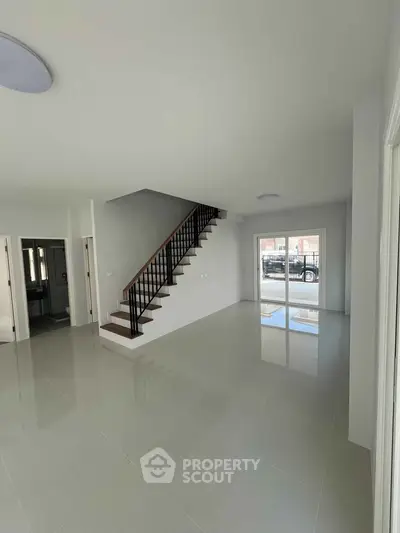 Spacious modern living room with sleek staircase and large windows for natural light.