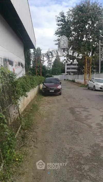 Entrance to a residential complex with parked cars and lush greenery.