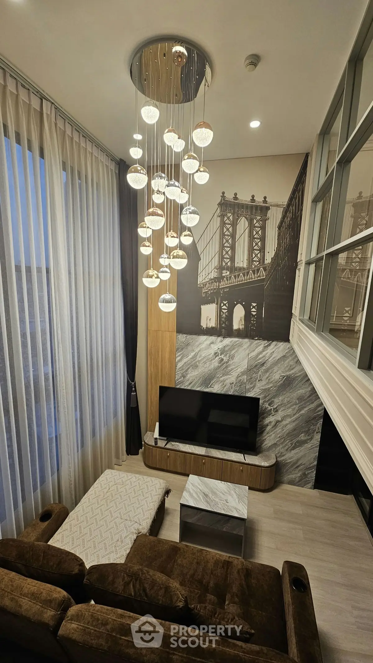 Luxurious living room with high ceilings, modern chandelier, and stylish decor featuring a large wall art of a bridge.