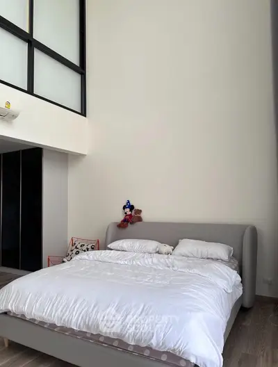 Spacious modern bedroom with high ceiling and cozy bed setup.