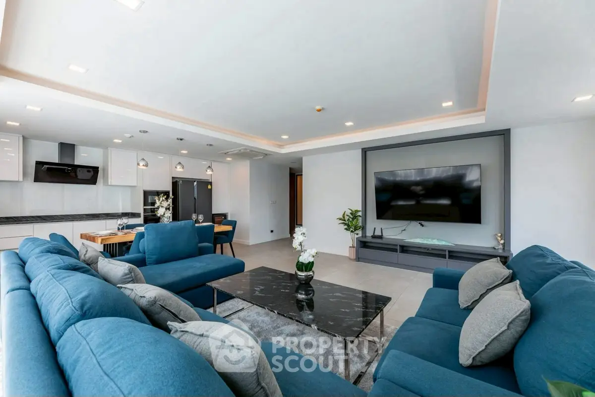 Luxurious open-plan living room with modern blue sofas and sleek kitchen area.