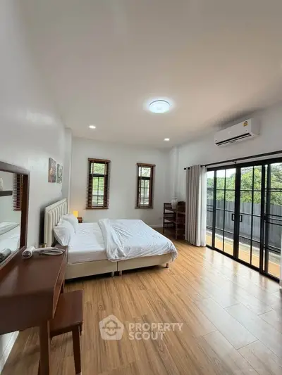 Spacious bedroom with balcony access and modern furnishings in a bright, airy setting.