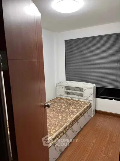 Cozy bedroom with modern decor and wooden flooring, featuring a comfortable bed and large window with blinds.