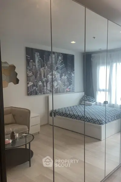 Modern bedroom with mirrored closet and cityscape artwork, featuring cozy seating and natural light.