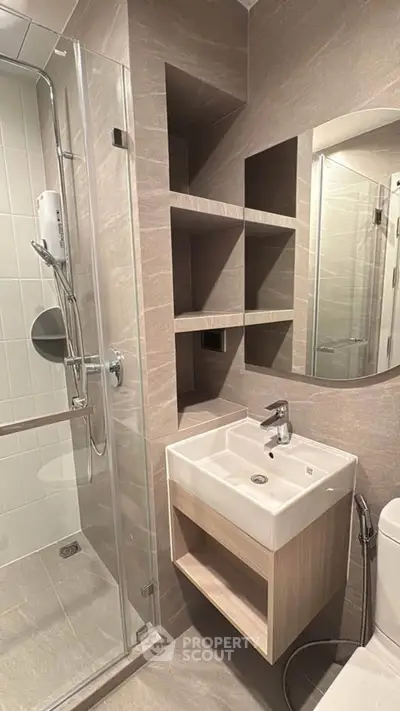Modern bathroom with sleek shower and compact sink in neutral tones.