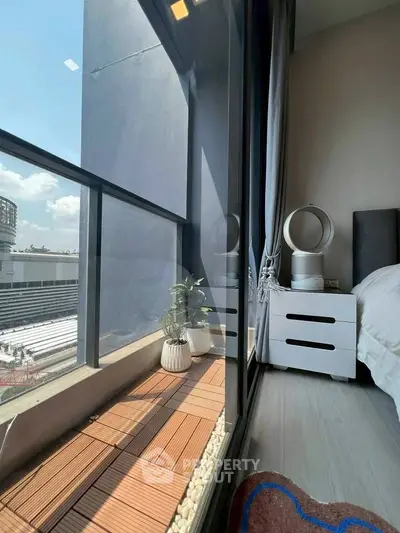 Modern bedroom with floor-to-ceiling windows and small balcony offering city views.