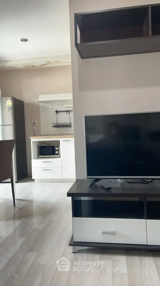 Modern living room with sleek TV unit and open kitchen layout, featuring contemporary appliances.