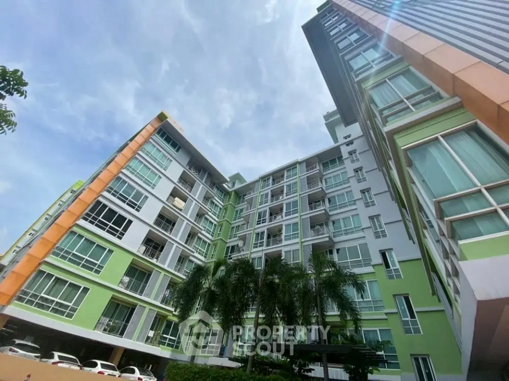Modern multi-story residential building with vibrant green facade and palm trees, showcasing urban living.