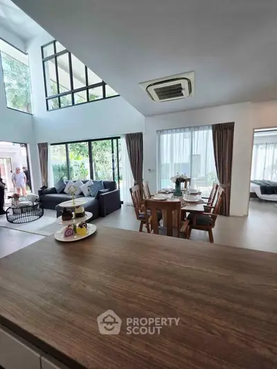 Spacious modern living room with high ceilings and large windows, featuring a cozy dining area and stylish decor.