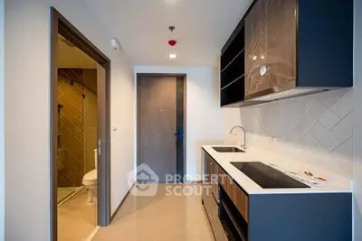 Modern apartment kitchen with sleek cabinetry and adjacent bathroom entrance.