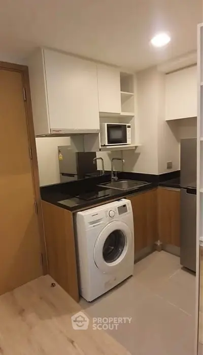 Modern compact kitchen with washing machine and microwave in a cozy apartment.