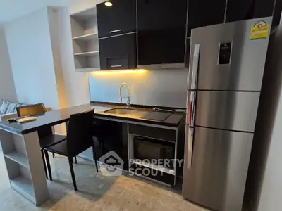 Modern kitchen with sleek black cabinets, stainless steel fridge, and cozy dining area.