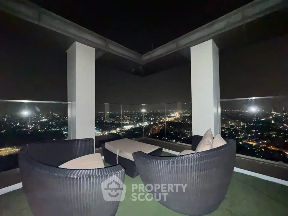 Stunning rooftop view with cozy seating overlooking city lights at night.