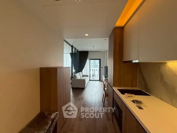 Modern apartment interior with open kitchen and cozy living area leading to a balcony with city view.