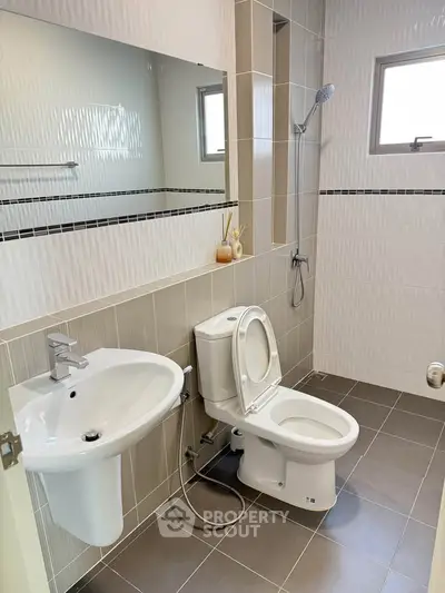 Modern bathroom with sleek fixtures and neutral tiles, featuring a shower and large mirror.