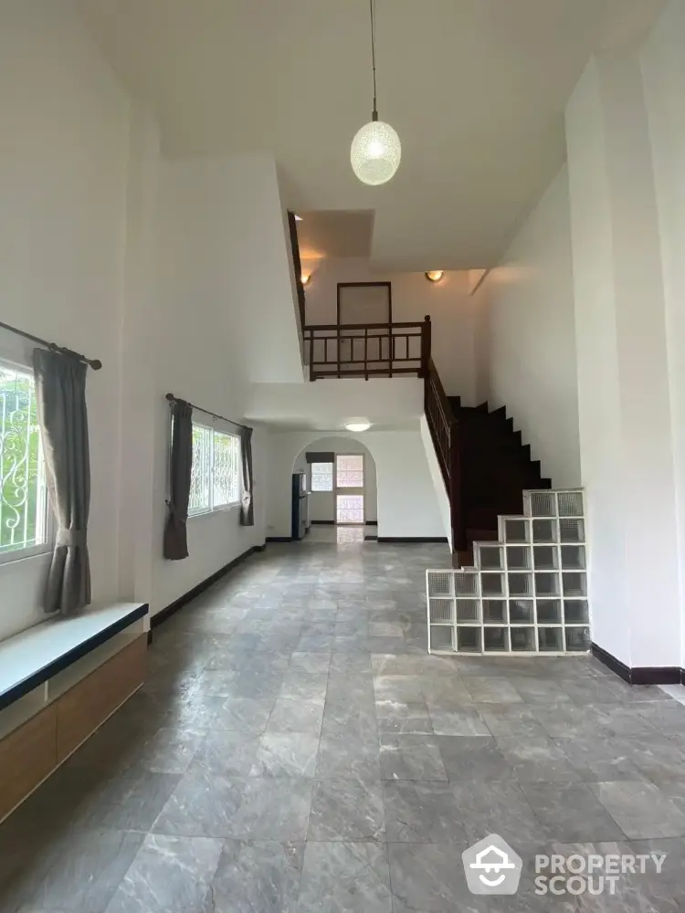 Spacious two-story home interior with high ceilings, natural light, and a grand staircase leading to an inviting mezzanine level.