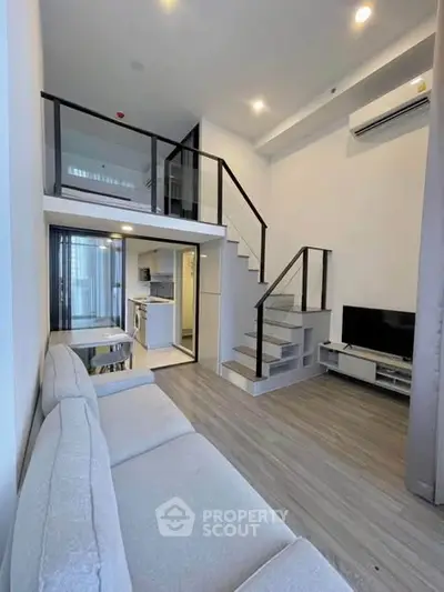 Modern loft-style living room with mezzanine, sleek staircase, and open kitchen layout.