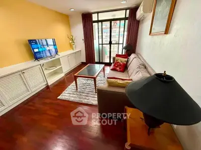 Cozy living room with wooden flooring, sofa, TV, and balcony access in a modern apartment.