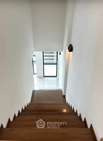 Modern staircase with wooden steps and sleek wall lighting leading to a bright landing area.