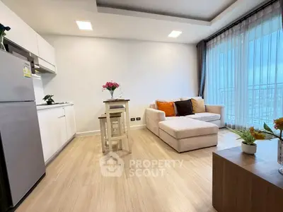 Modern living room with open kitchen and cozy seating area, featuring large windows and stylish decor.