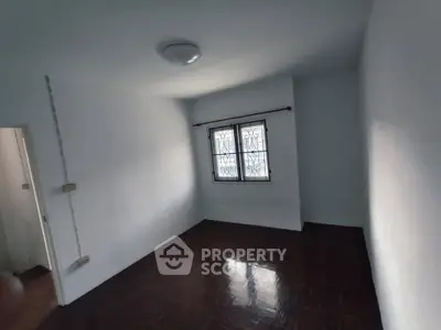 Spacious empty room with wooden flooring and natural light from window.