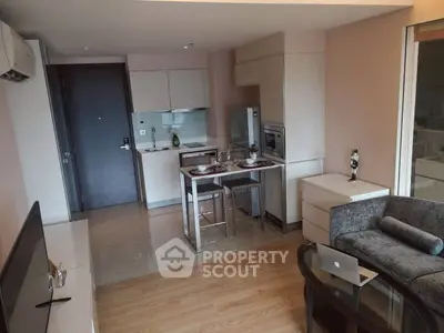 Modern open-layout living room with kitchen, featuring sleek furniture and natural lighting.