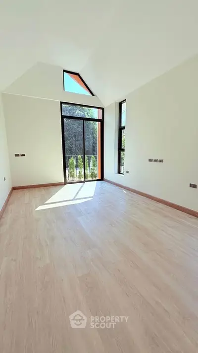 Spacious empty room with large windows and high ceiling, offering abundant natural light and serene garden view.