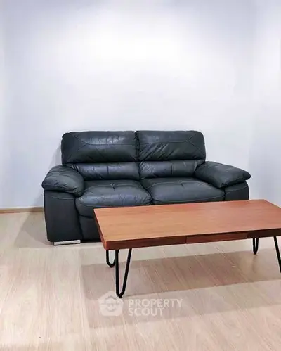 Modern living room with sleek black leather sofa and stylish wooden coffee table.
