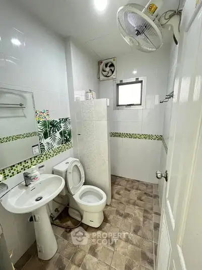 Compact bathroom with modern fixtures and tiled walls, featuring a fan and small window for ventilation.