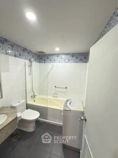 Modern bathroom with bathtub and washing machine, featuring stylish tile accents.