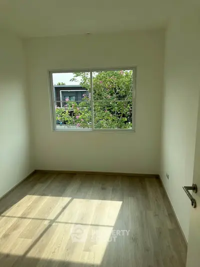 Bright empty room with large window and wooden flooring, perfect for customization.
