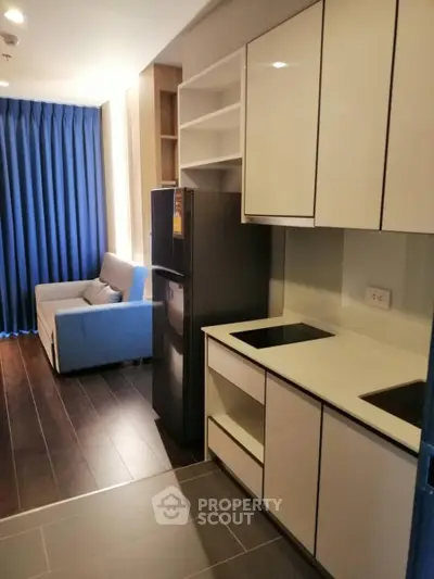 Modern kitchen with sleek cabinetry and cozy living area in open layout apartment.