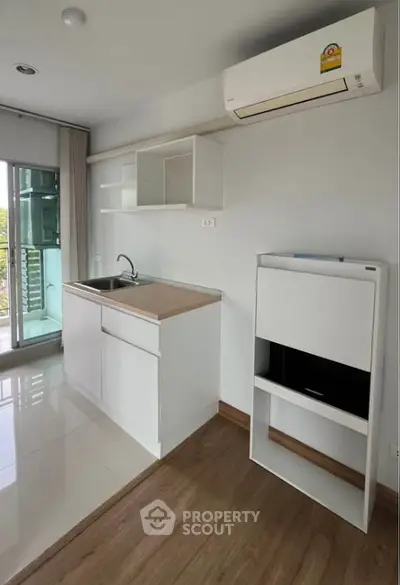Modern compact kitchen with sleek white cabinets and air conditioning, featuring a bright balcony view.