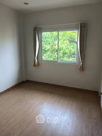 Bright empty room with wooden flooring and large window overlooking greenery.