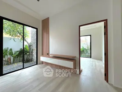 Spacious modern living room with large windows and garden view, featuring sleek wooden accents and light flooring.