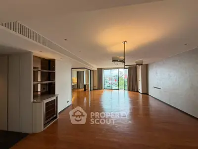 Spacious modern living room with wooden flooring and large windows offering city views.