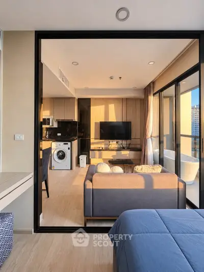 Modern open-plan living room with kitchen and washing machine, featuring a cozy sofa and large windows.
