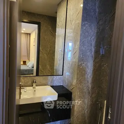 Luxurious marble bathroom with modern sink and mirror, adjacent to a cozy bedroom.