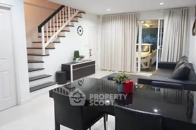 Modern living room with sleek black dining table and staircase, adjacent to a glass door leading to a garage.