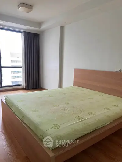 Spacious bedroom with large window and modern wooden bed frame in a bright apartment.