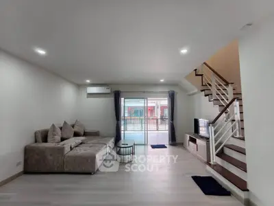 Spacious modern living room with cozy sofa and staircase, featuring natural light and stylish decor.