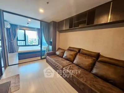 Modern living room with brown sofa and glass partition leading to bedroom