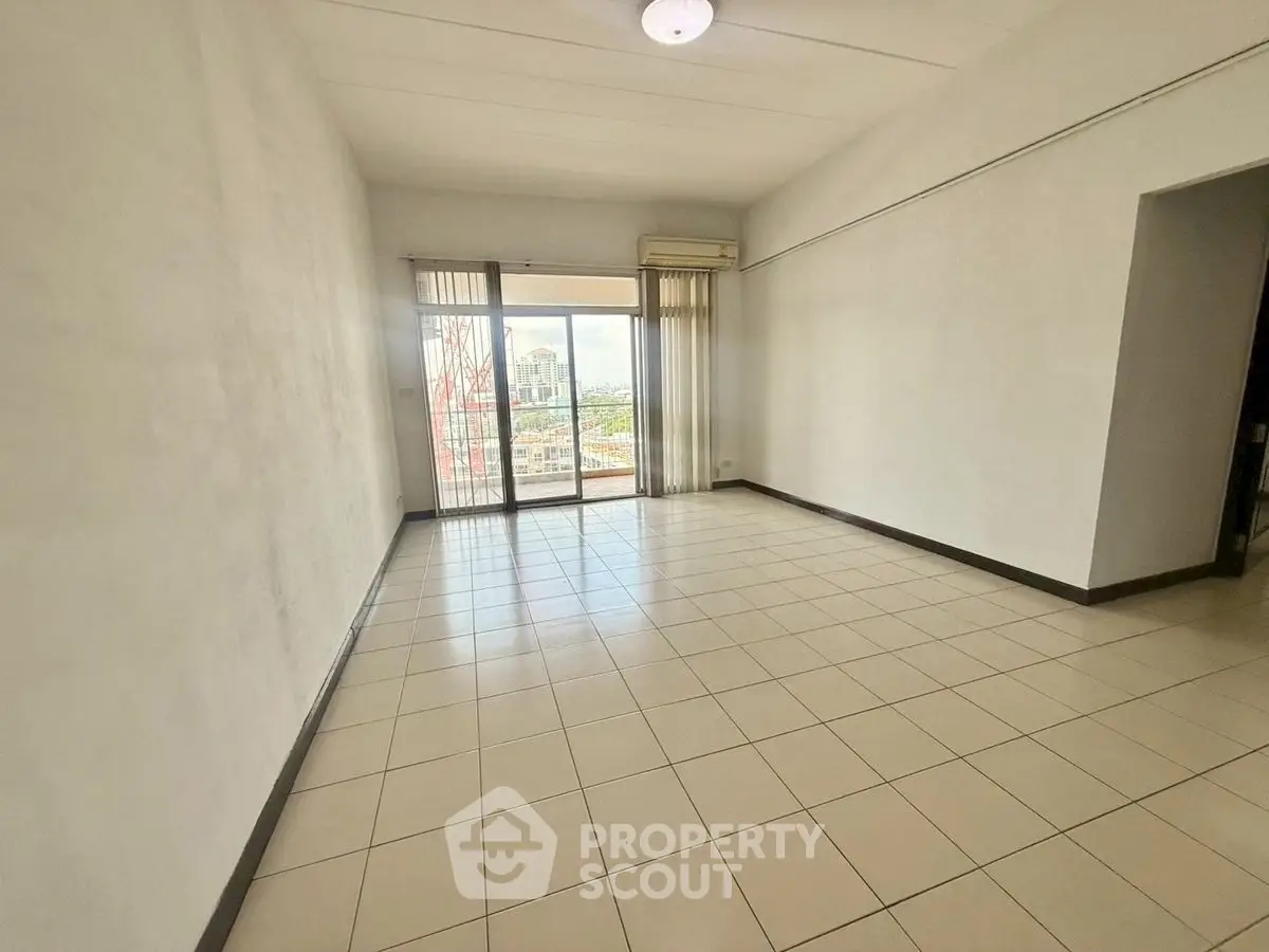 Spacious empty living room with tiled floors and balcony view in urban apartment.
