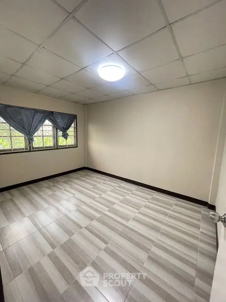 Spacious empty room with tiled flooring and large window, perfect for customization.